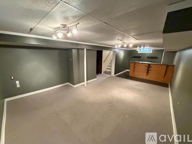 A spacious room with a grey carpet and a wooden cabinet in the corner.