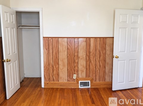 A room with a white door, a white wall, and a wooden floor with a vent.