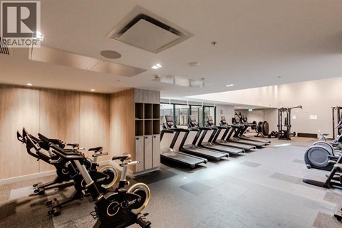 A gym with a row of stationary bikes and a row of treadmills.