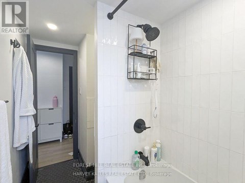 A white tiled bathroom with a towel hanging on the door.