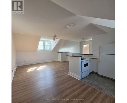 A real estate listing photo of a kitchen and living room with wood floors and white walls.