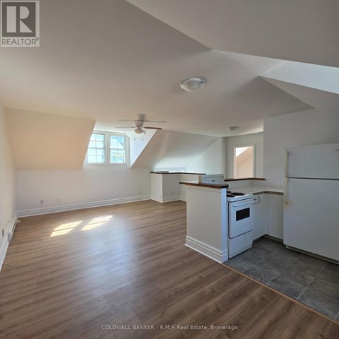 A real estate listing photo of a kitchen and living room with wood floors and white walls.