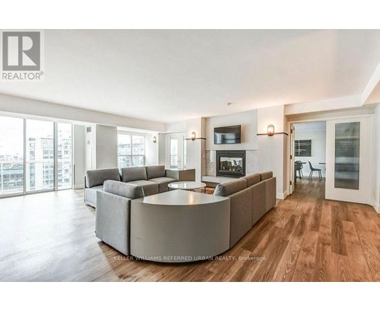 A spacious living room with a large grey sofa and a television on the wall.