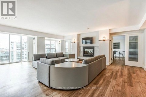 A spacious living room with a large grey sofa and a television on the wall.