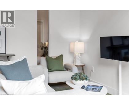 A living room with a white couch, a small table with a plant, and a flat-screen TV mounted on the wall.