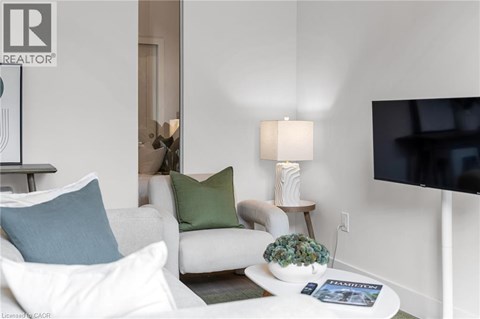 A living room with a white couch, a small table with a plant, and a flat-screen TV mounted on the wall.