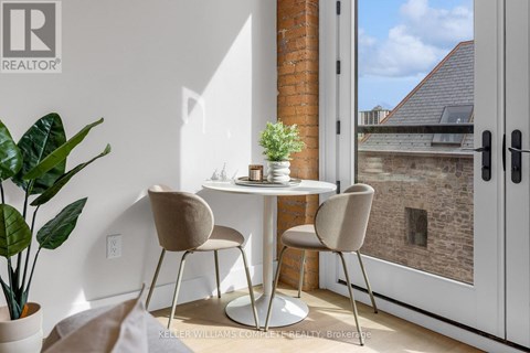 A table with two chairs and a potted plant sits in a room with a view of a brick building outside.