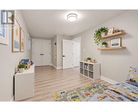 A well-lit, spacious room with a bed, a cabinet, and a shelf with plants and picture frames.