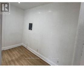 A room with a wooden floor and white walls, with a black object on the wall.