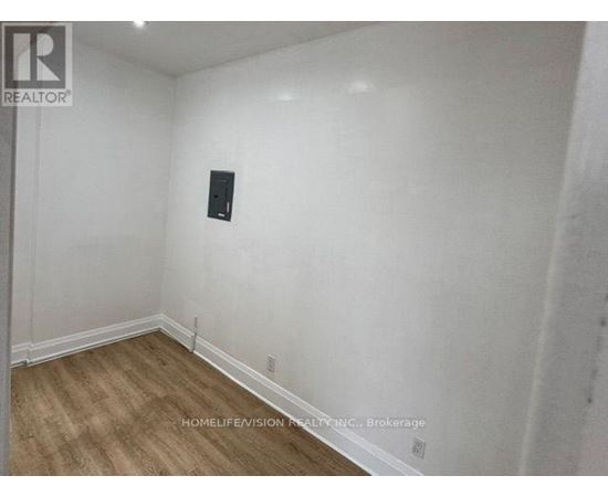 A room with a wooden floor and white walls, with a black object on the wall.