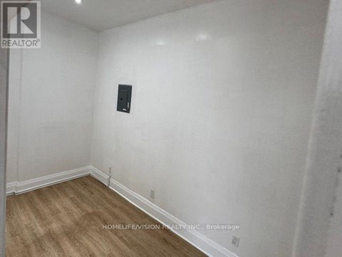 A room with a wooden floor and white walls, with a black object on the wall.