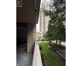 A building with a balcony overlooking a garden with a tall building in the background.