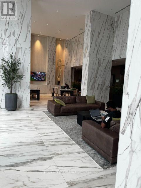 A man is sitting on a couch in a spacious lobby with marble floors and walls.