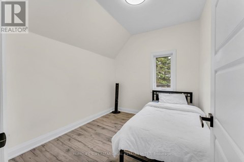 A bedroom with a bed, wooden floor, and a window with a view of trees.