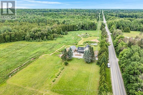 A road runs through a green field with a house on the right side.