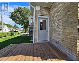 A wooden deck leads to a white door on a brick house.