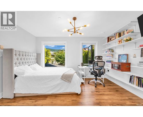 A bedroom with a large bed, a desk with a chair, and a window with a view of the outdoors.