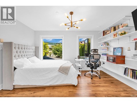 A bedroom with a large bed, a desk with a chair, and a window with a view of the outdoors.
