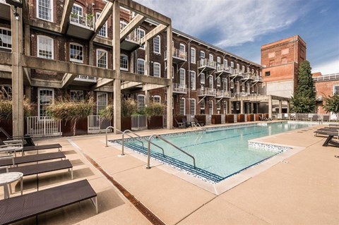 A large outdoor swimming pool surrounded by sun loungers and a building with balconies.