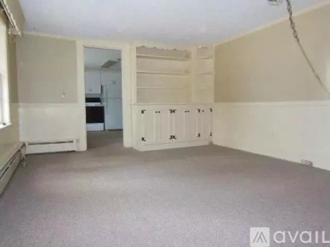A spacious room with a white door and a window on the left.