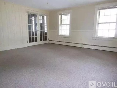 A room with white walls and carpeted floor with two windows.