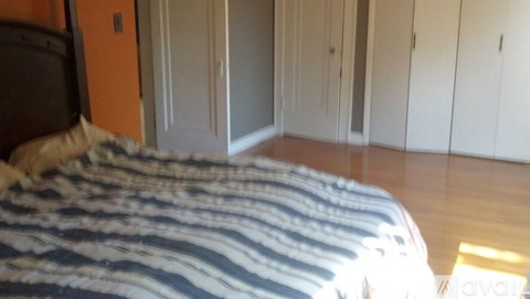 A bed with a striped comforter sits in a room with wooden floors and white walls.