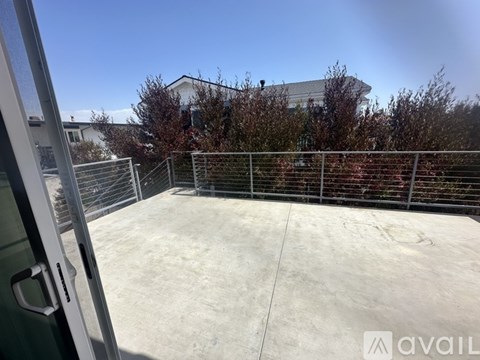 A view from inside a building looking out to a concrete patio with a metal fence and trees in the background.