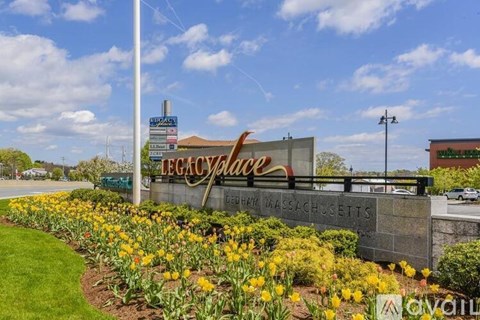 A sign that says Legacy Place in front of a field of yellow flowers.