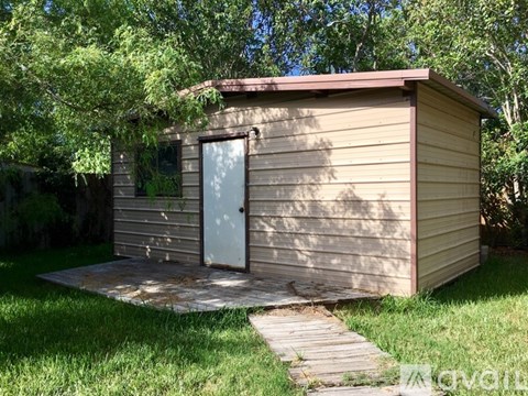 A small wooden shed with a white door and a wooden walkway leading to it.