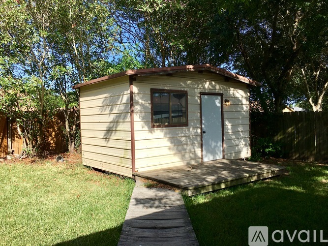 A small house with a white door and a brown roof is surrounded by trees.