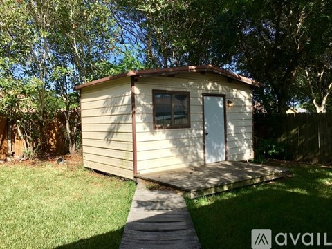 A small house with a white door and a brown roof is surrounded by trees.