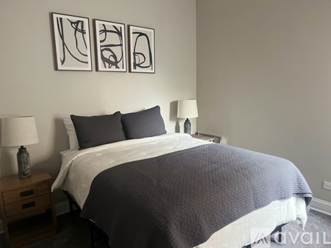 A bed with a grey comforter and two pillows sits in a room with two lamps on either side.