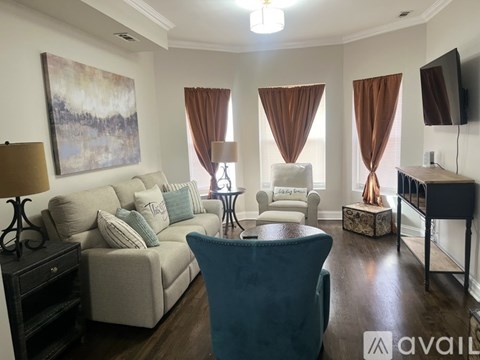 A living room with a blue chair in the foreground and a painting on the wall.