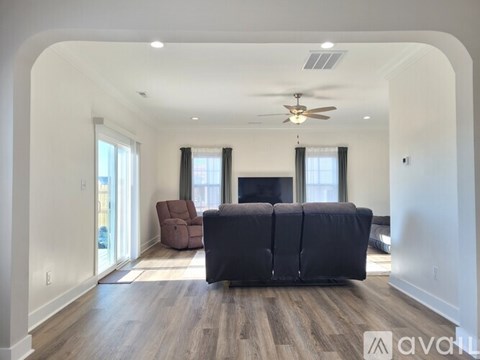 A spacious living room with a black couch and a ceiling fan.