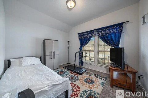 A bedroom with a bed, a TV, and a window with curtains.