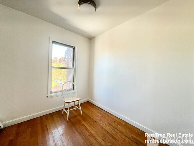 A room with a wooden floor and a window with a chair in it.