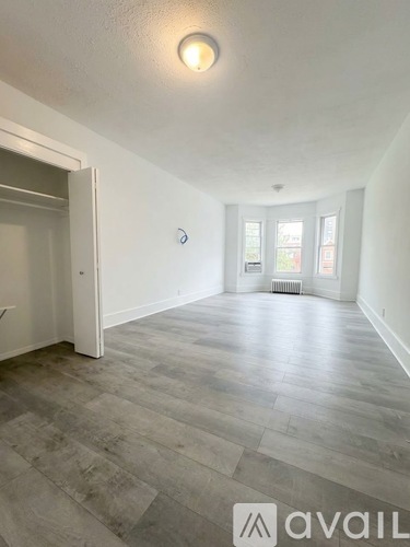 A room with a grey floor and white walls, with a door on the left and a window on the right.