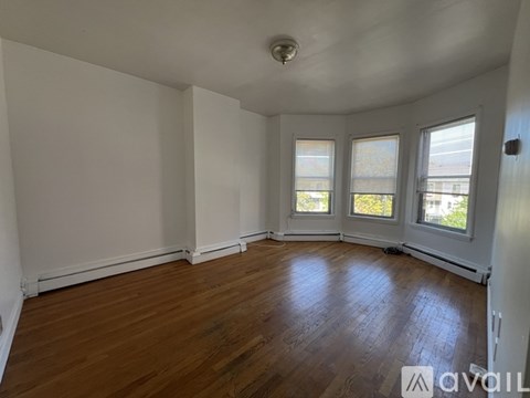 A room with wooden floors and white walls has a window with a view of trees.