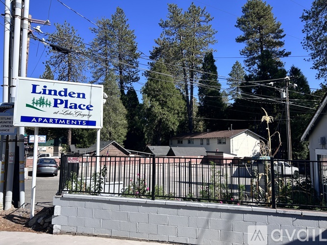 A sign for Linden Place Apartments is in front of a fence and some houses.