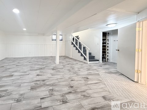 A spacious room with a staircase and a door on the right.