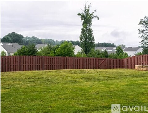 A grassy field with a wooden fence in the foreground and houses in the background.