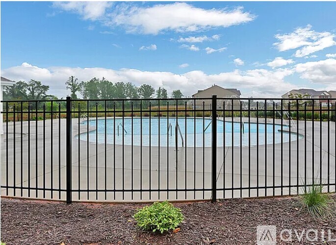 A black fence surrounds a pool with a house and trees in the background.