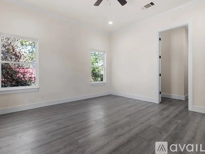 A spacious room with a ceiling fan and two windows.