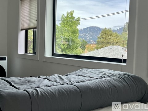 A bed with a grey cover is in front of a window with a view of trees and a mountain.