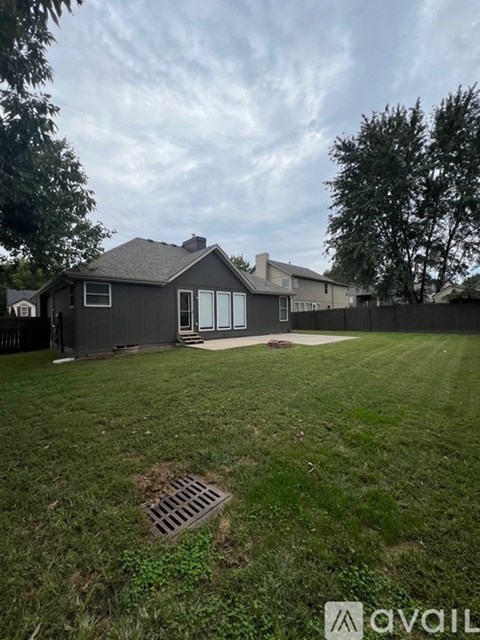 A house with a grey roof and a white fence is surrounded by a grassy yard.