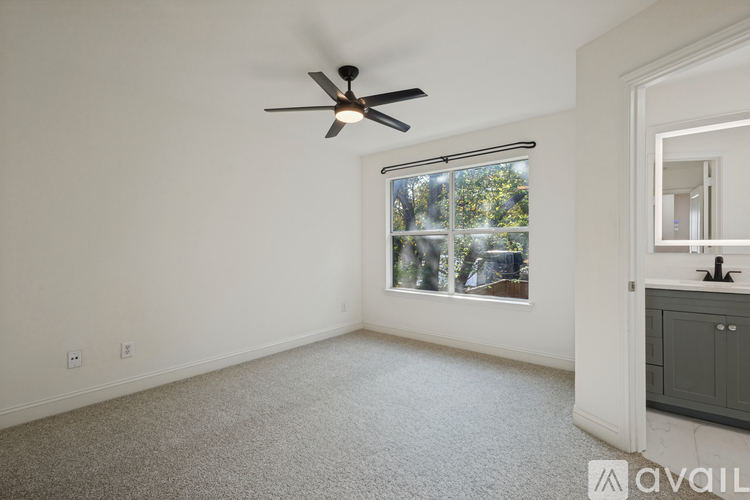A room with a ceiling fan and a window with a view of trees.