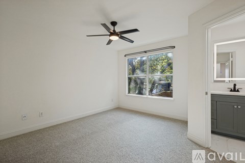 A room with a ceiling fan and a window with a view of trees.