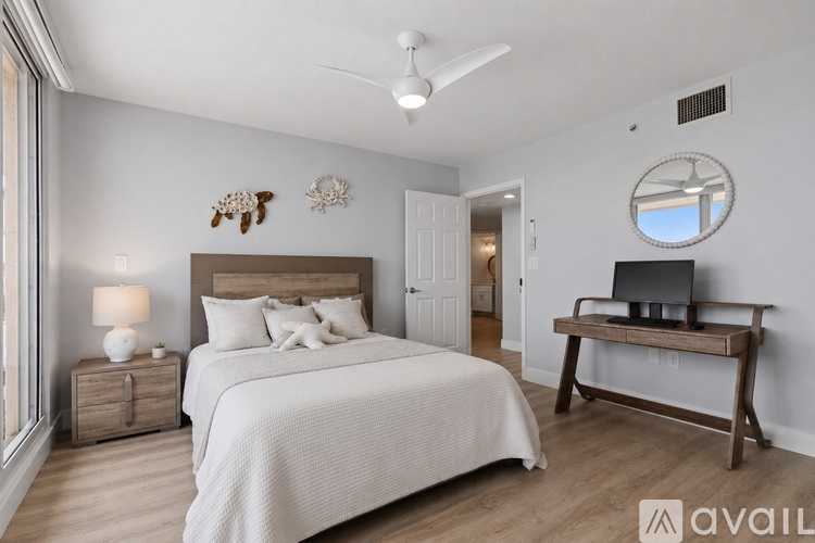 A bedroom with a large bed, a nightstand with a lamp, a bench with a TV on it, and a round mirror on the wall.