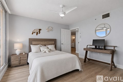 A bedroom with a large bed, a nightstand with a lamp, a bench with a TV on it, and a round mirror on the wall.