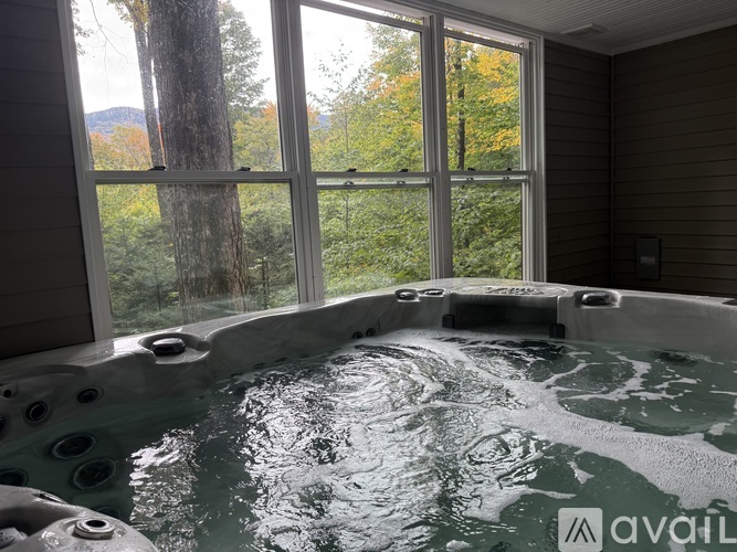 A hot tub in a room with a view of the forest.